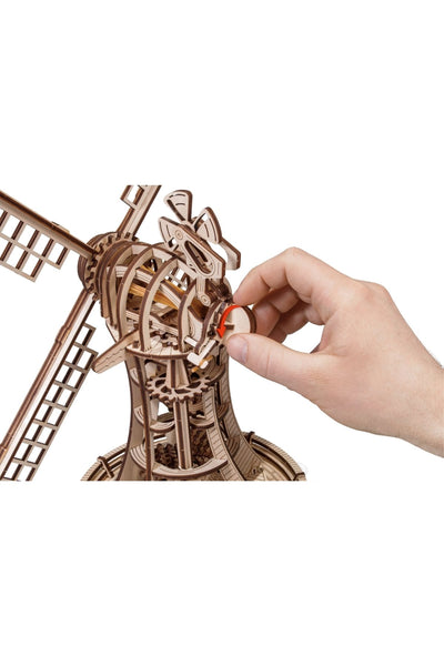 Eine Hand verstellt einen kleinen Holzhebel an einem detaillierten Holzmodell einer Windmühle.