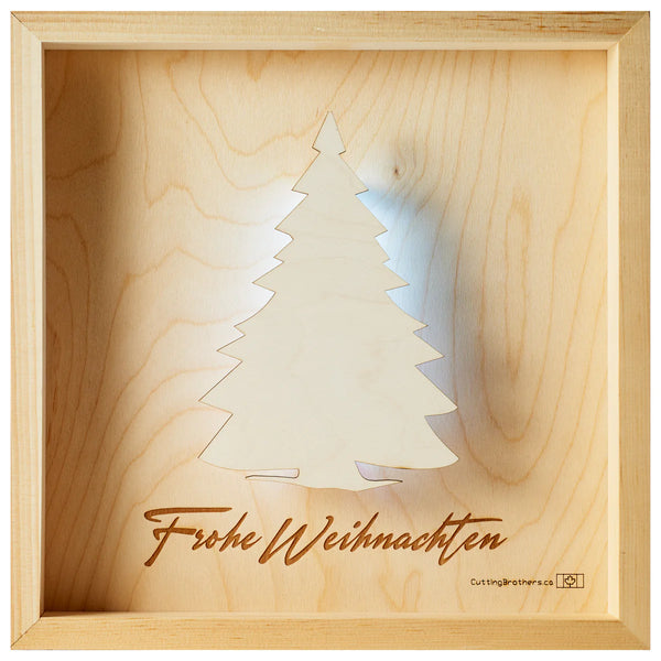Holzkunstwerk mit ausgeschnittenem Weihnachtsbaum und darunter eingraviertem Frohe Weihnachten, in einem Holzrahmen.