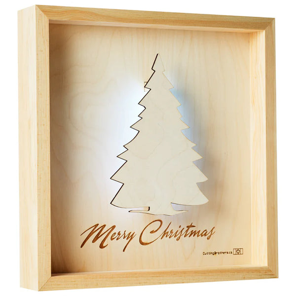 Gerahmtes Kunstwerk aus Holz mit einem ausgeschnittenen Weihnachtsbaum und der Gravur Merry Christmas darunter.