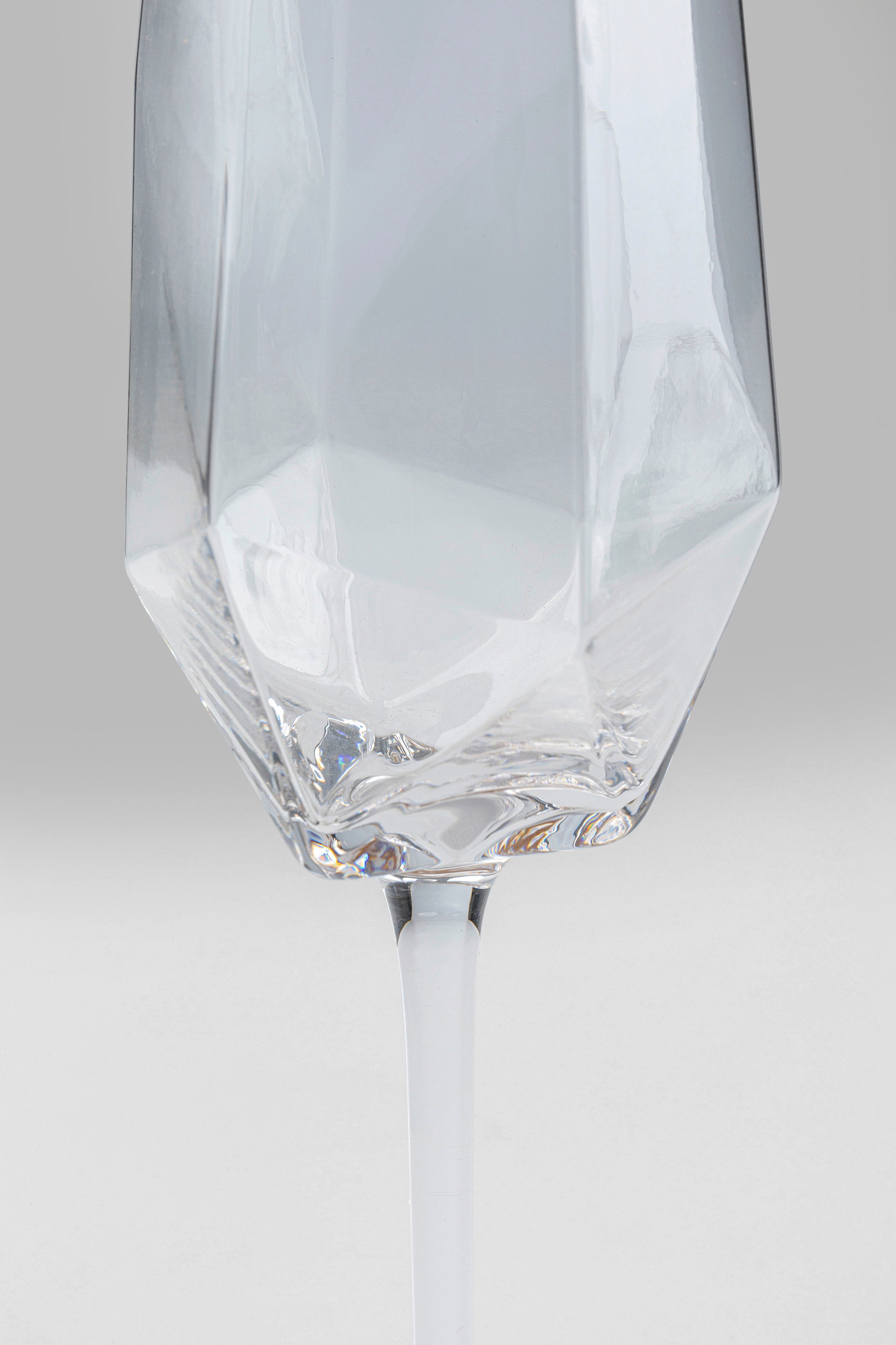 Nahaufnahme eines Sektglases Diamond Gold Rim (4/tlg.) mit geometrischen Facetten und langem Stiel, gefüllt mit Wasser, vor hellgrauem Hintergrund.