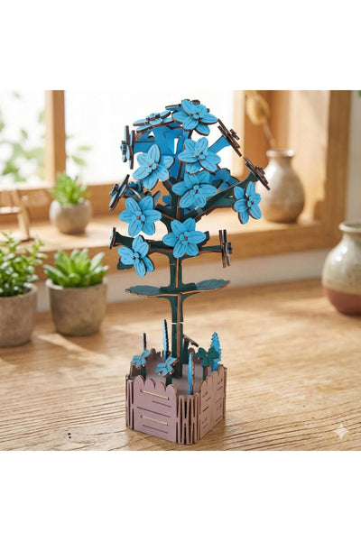 Ein Holzmodell eines blauen Blumenbaums mit einem braunen Zaunfuß steht auf einem Tisch, im Hintergrund stehen Topfpflanzen und Vasen.