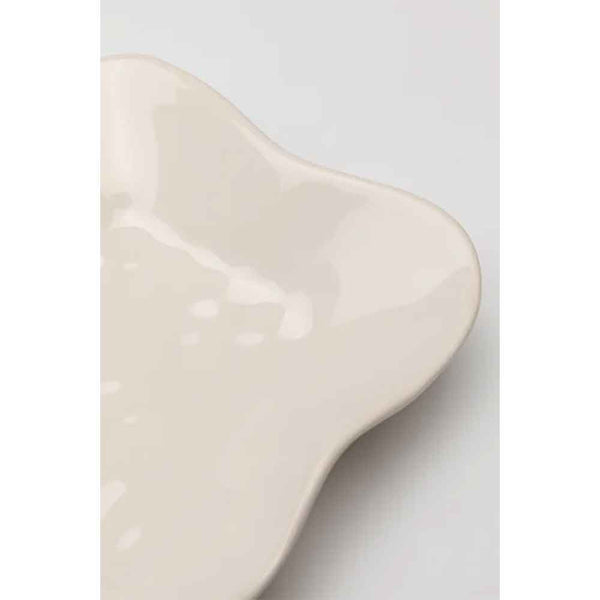 Abstrakter cremefarbener Keramikteller mit gewelltem Rand auf hellem Hintergrund.