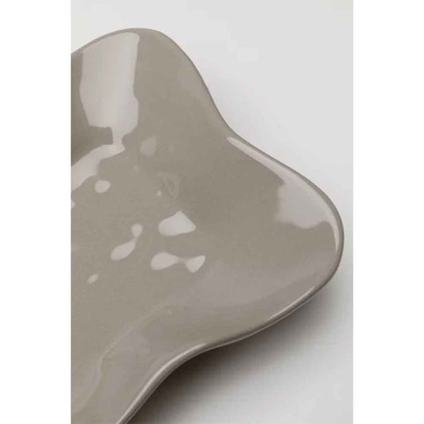 Geschwungener, taupefarbener Keramikteller mit unregelmäßiger, organischer Form auf weißem Grund.