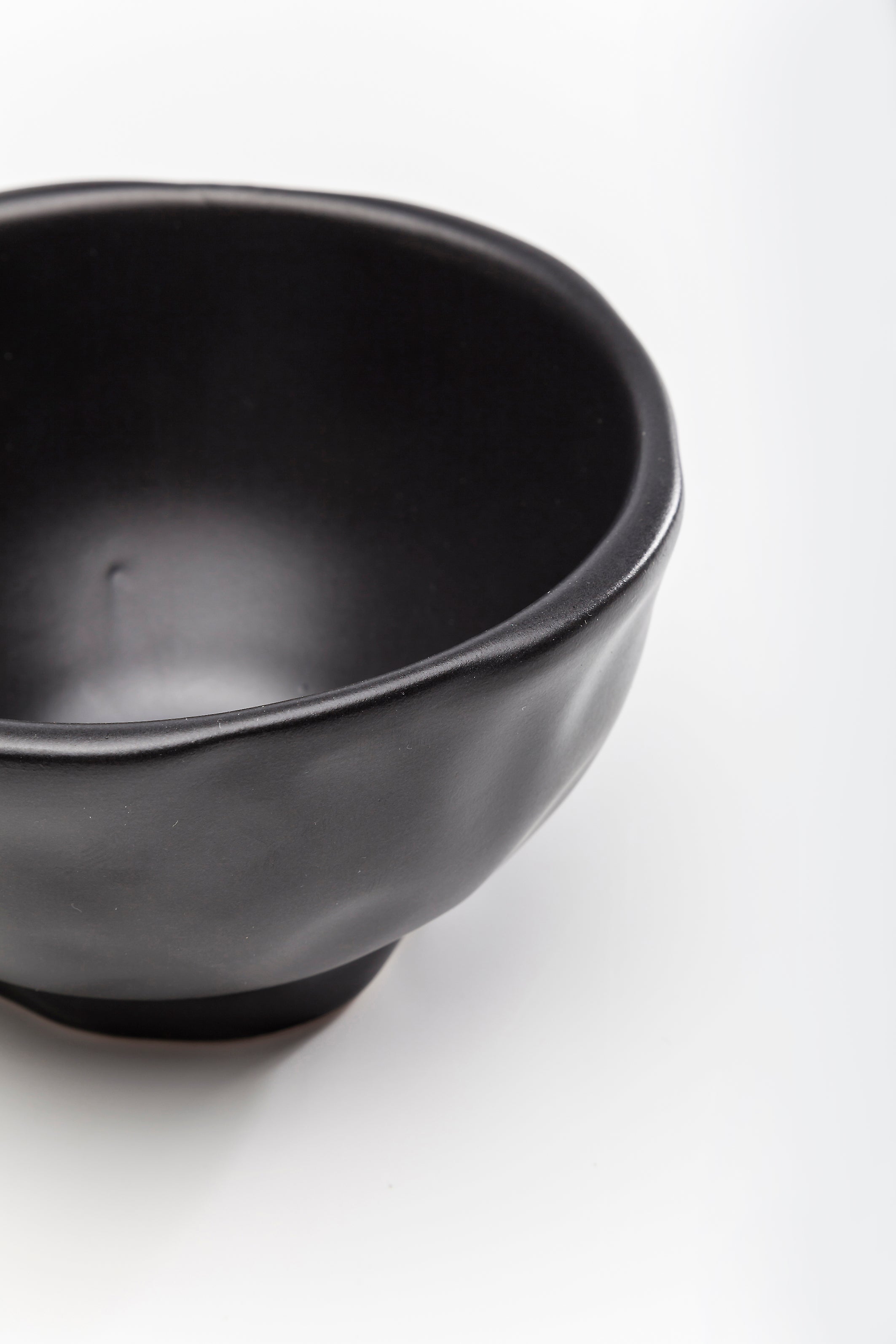 Eine Nahaufnahme der Schale Organic Black Ø15cm – eine einfache, mattschwarze Schale mit sanften Rundungen – vor einem schlichten weißen Hintergrund.