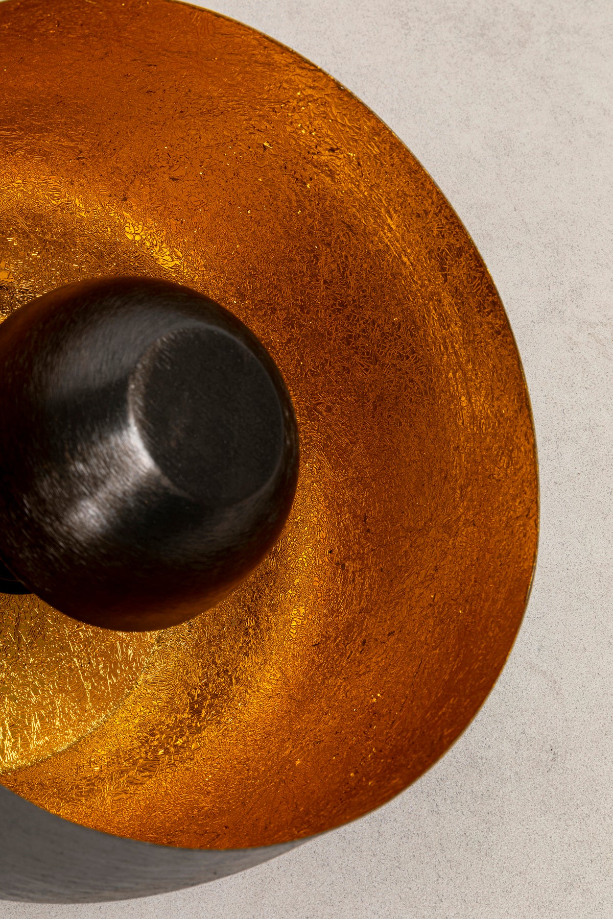 Nahaufnahme der strukturierten goldenen Oberfläche und der glatten dunklen Mitte der Bodenleuchte Apollon Smooth Ø28cm, die an ihre effektvolle Beleuchtung erinnert, fotografiert vor einem hellen, neutralen Hintergrund.