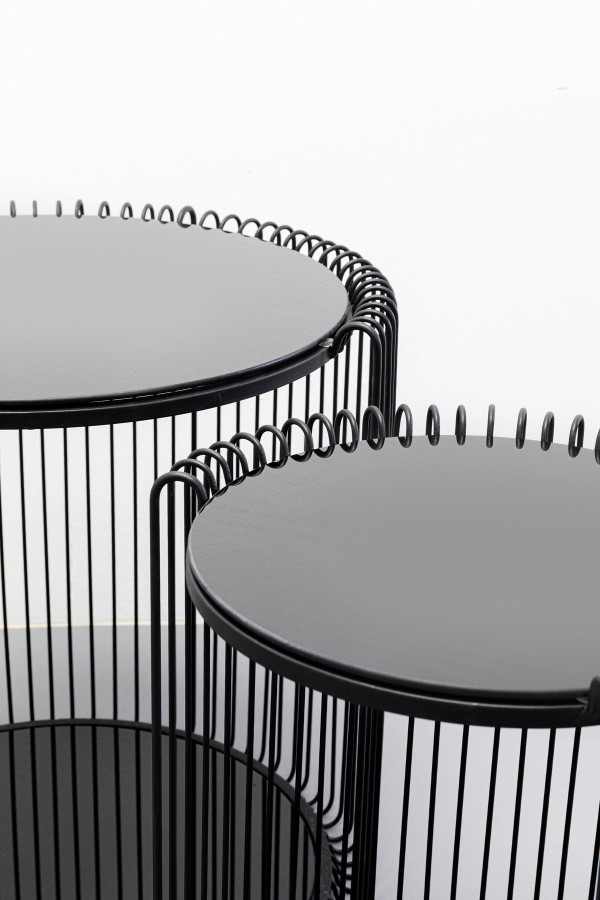 Nahaufnahme des Beistelltischs Wire Double Schwarz (2/Set) mit modernen Drahtrahmenbasen und glatten Sicherheitsglasplatten, die in unterschiedlichen Höhen vor einem weißen Hintergrund präsentiert werden.