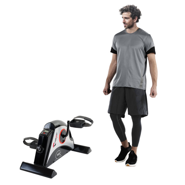 Ein Mann in Sportkleidung steht neben einem kompakten Pedaltrainingsgerät auf weißem Hintergrund.