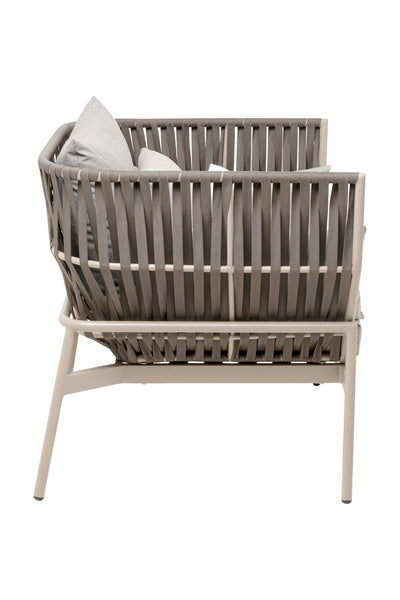 Seitenansicht eines modernen Loungesessels für den Außenbereich mit beigem Metallrahmen, breiter geflochtener Rückenlehne und Seiten sowie grauen Sitz- und Rückenkissen.