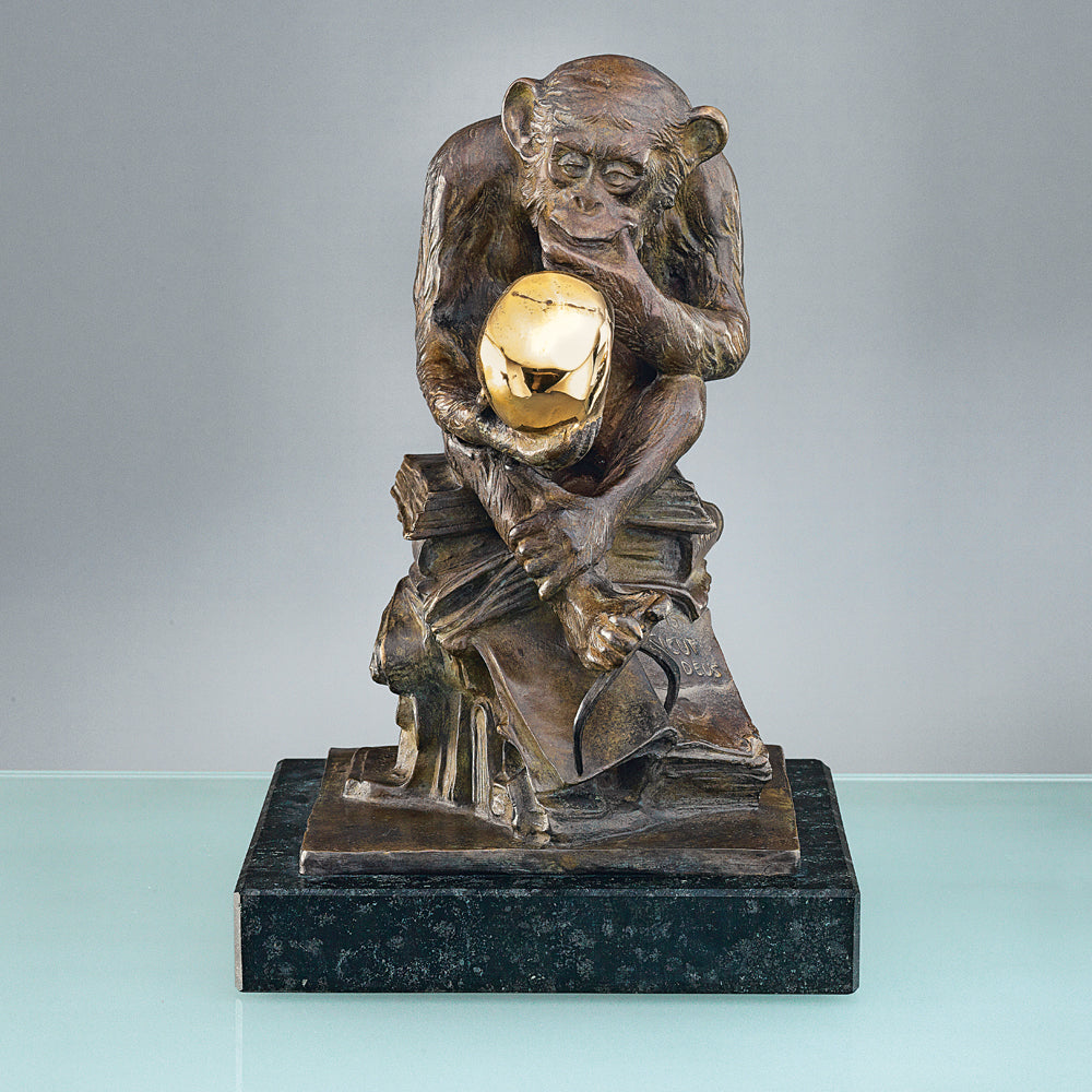Bronzene Affenskulptur auf Büchern, die eine glänzende goldene Kugel auf einem schwarzen Sockel hält und anstarrt.