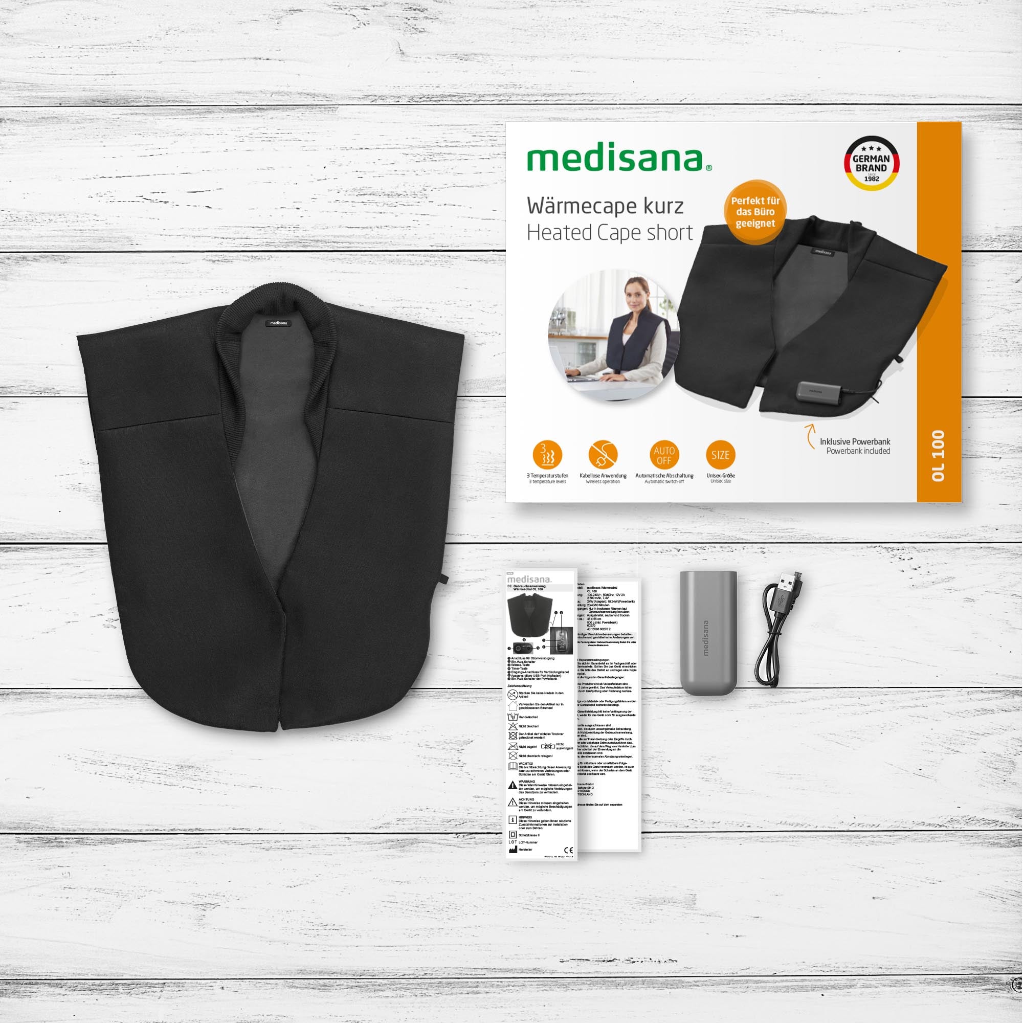Beheizter schwarzer Schulterumhang mit Verpackung, Bedienungsanleitung, Powerbank und USB-Kabel auf weißem Holzhintergrund.