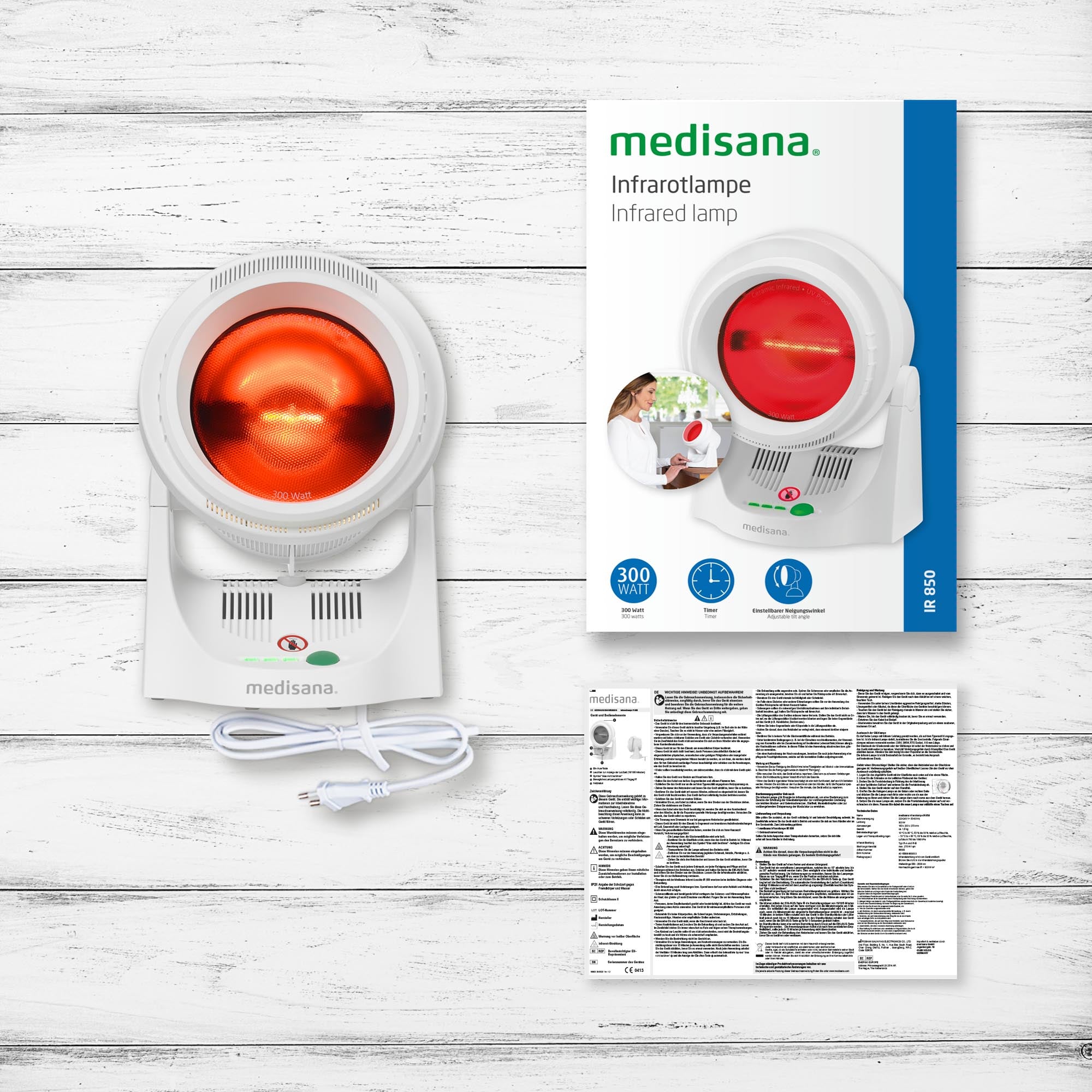 Medisana Infrarotlampe mit Kabel, Verpackungskarton und Gebrauchsanweisung auf weißer Holzoberfläche.
