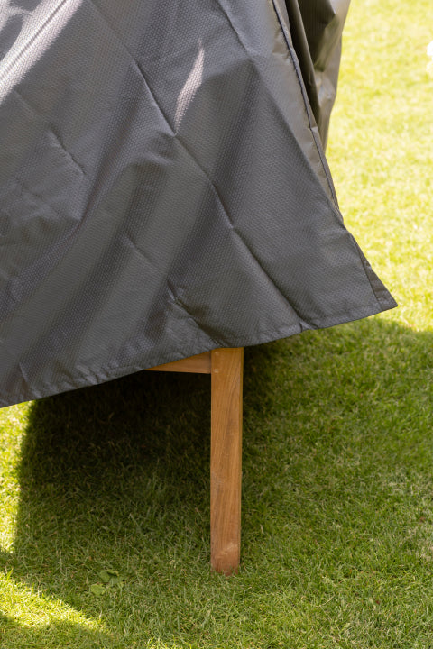 Eine graue wetterfeste Abdeckung, die über ein hölzernes Möbelbein auf grünem Gras drapiert ist.