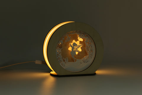 Eine runde Dekolampe mit leuchtendem Feen- und Blumendesign, die einen dunklen Hintergrund sanft beleuchtet.