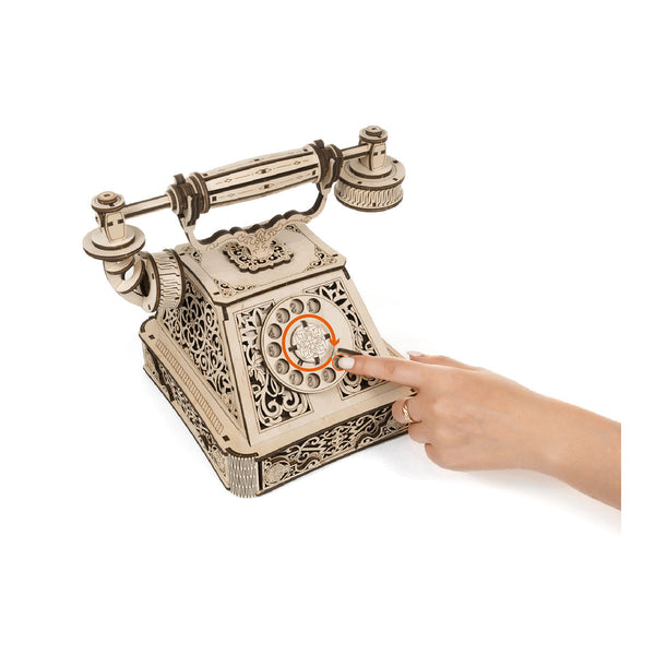 Eine Hand wählt ein hölzernes Wählscheibenmodell im Vintage-Stil mit komplizierten Ausschnitten.