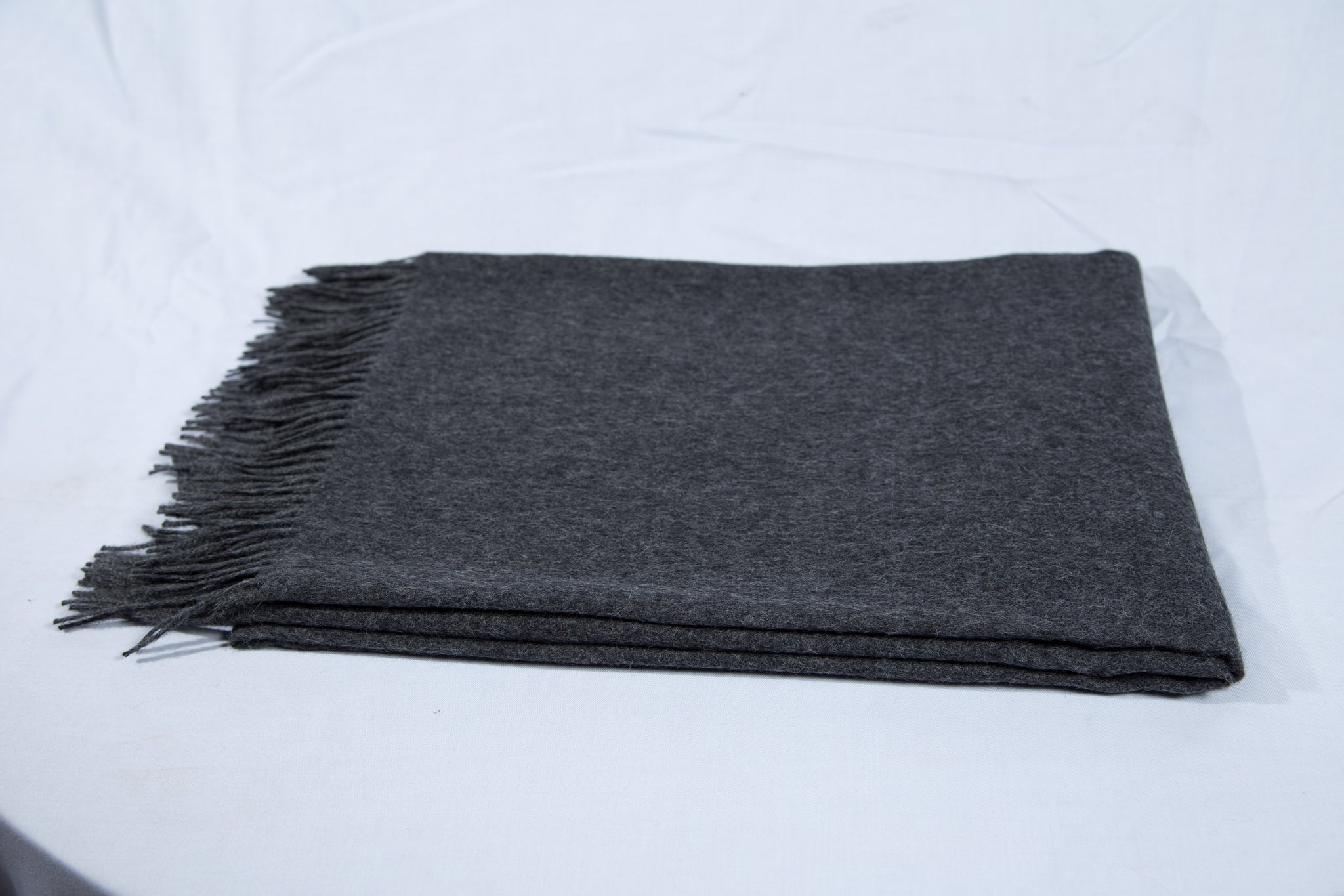 Ein ordentlich gefalteter dunkelgraue Decke mit ausgefransten Rändern auf weißem Hintergrund.