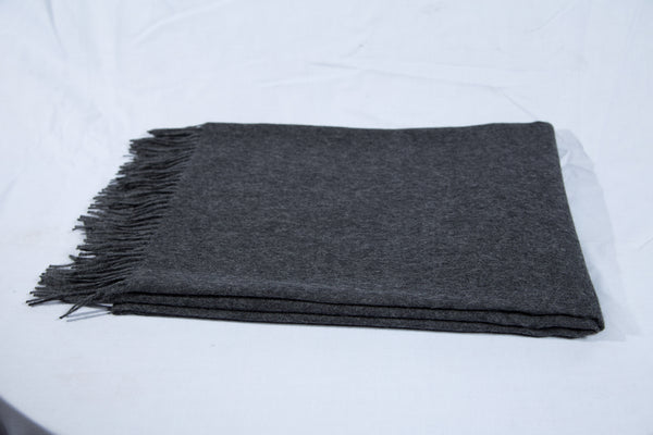 Ein ordentlich gefalteter dunkelgraue Decke mit ausgefransten Rändern auf weißem Hintergrund.