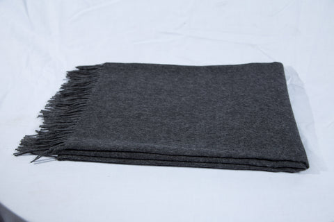 Ein ordentlich gefalteter dunkelgraue Decke mit ausgefransten Rändern auf weißem Hintergrund.