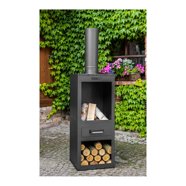 Schwarzer Kaminofen mit Schornstein, darunter gelagerte Holzscheite, auf einer Steinterrasse an einer mit Efeu bewachsenen Mauer.