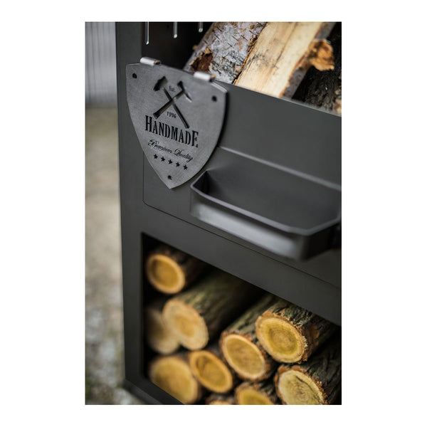 Nahaufnahme von gestapeltem Brennholz in einem schwarzen Metallhalter mit einer handgefertigten Metallplakette auf der Vorderseite.