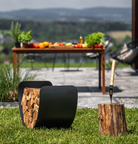 Ein mit Brennholz gefüllter Holzscheithalter und eine Axt in einem Baumstumpf, mit einem gedeckten Tisch zum Essen im Freien.