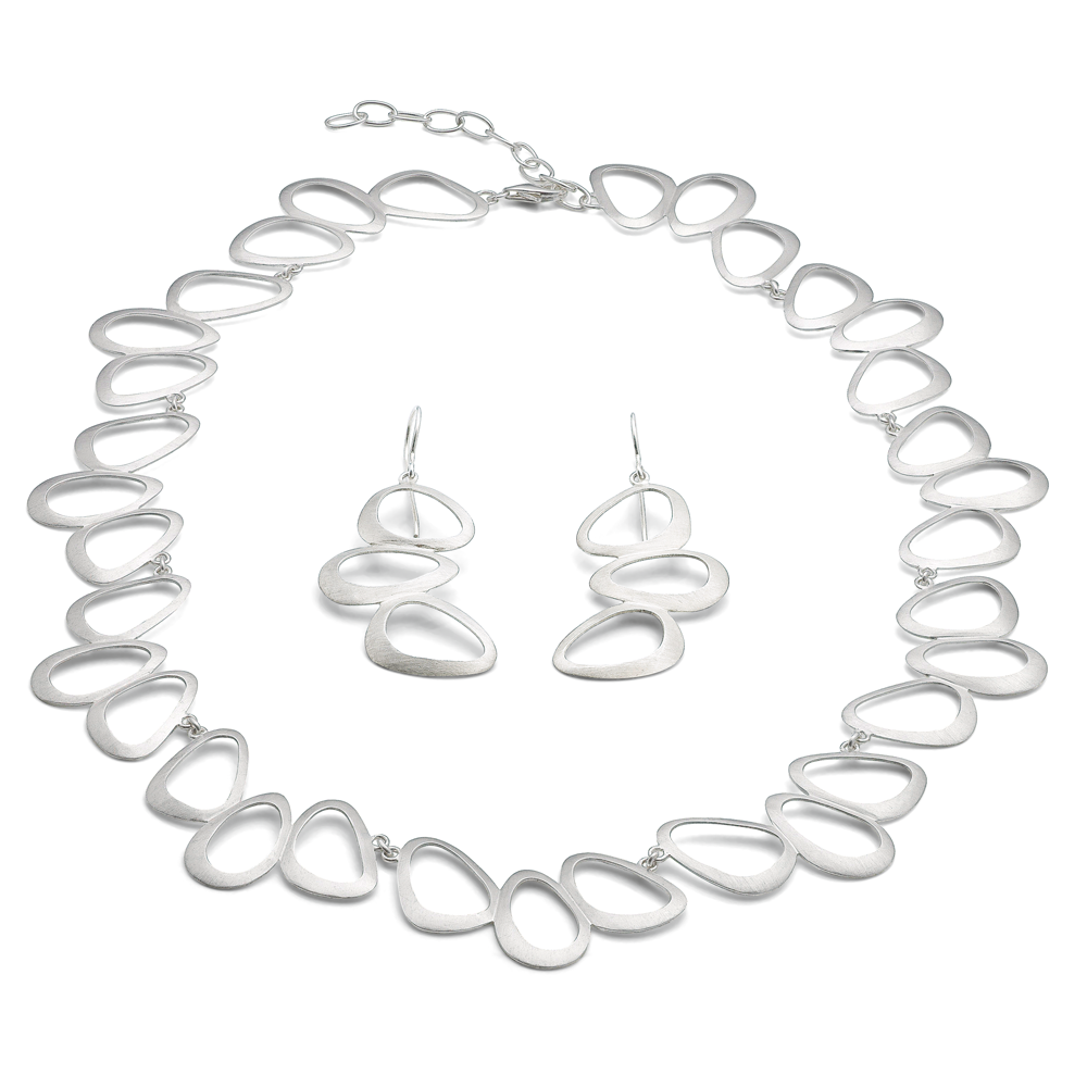 Judith Martini: Das Schmuckset „Petit Bijou“ besteht aus einer silbernen Halskette und passenden Ohrringen mit abstrakten, offenen, tropfenförmigen Gliedern auf weißem Hintergrund.