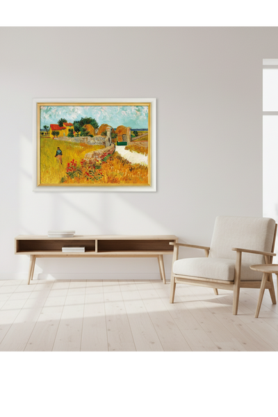 Das Gemäldem auf dem eine Person unter blauem Himmel durch ein Feld mit Heuhaufen geht, einer Steinmauer und einem gelben Haus, eingebettet in einen Wohnraum mit Sofa und Kommode. 