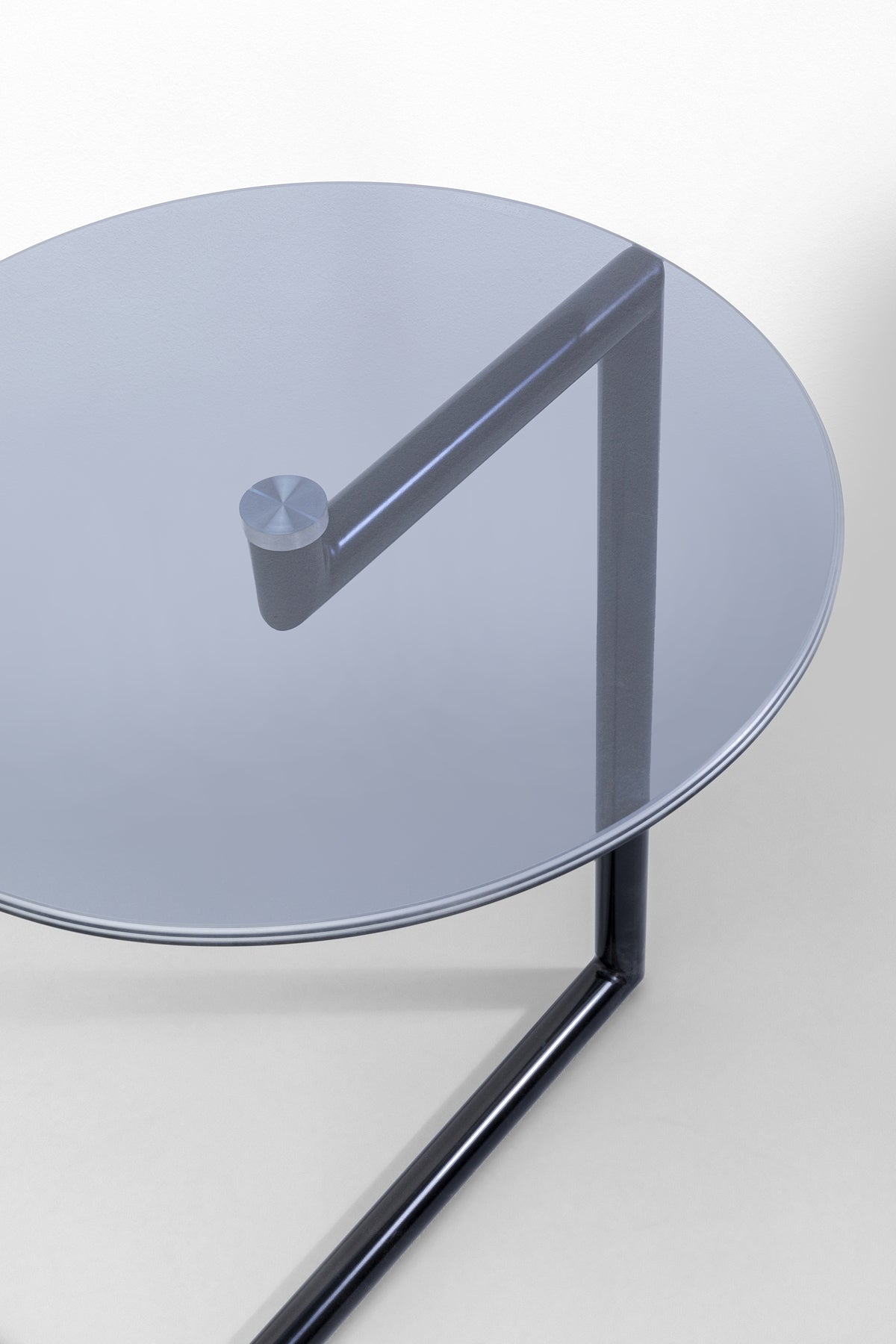 Der Beistelltisch Easy Living Schwarz Ø46 cm verfügt über eine runde Glasplatte, einen dunklen Metallrahmen und eine einzelne zylindrische Seitenstütze und bietet ein zeitloses Design, das sich wunderschön von einem hellen Hintergrund abhebt.