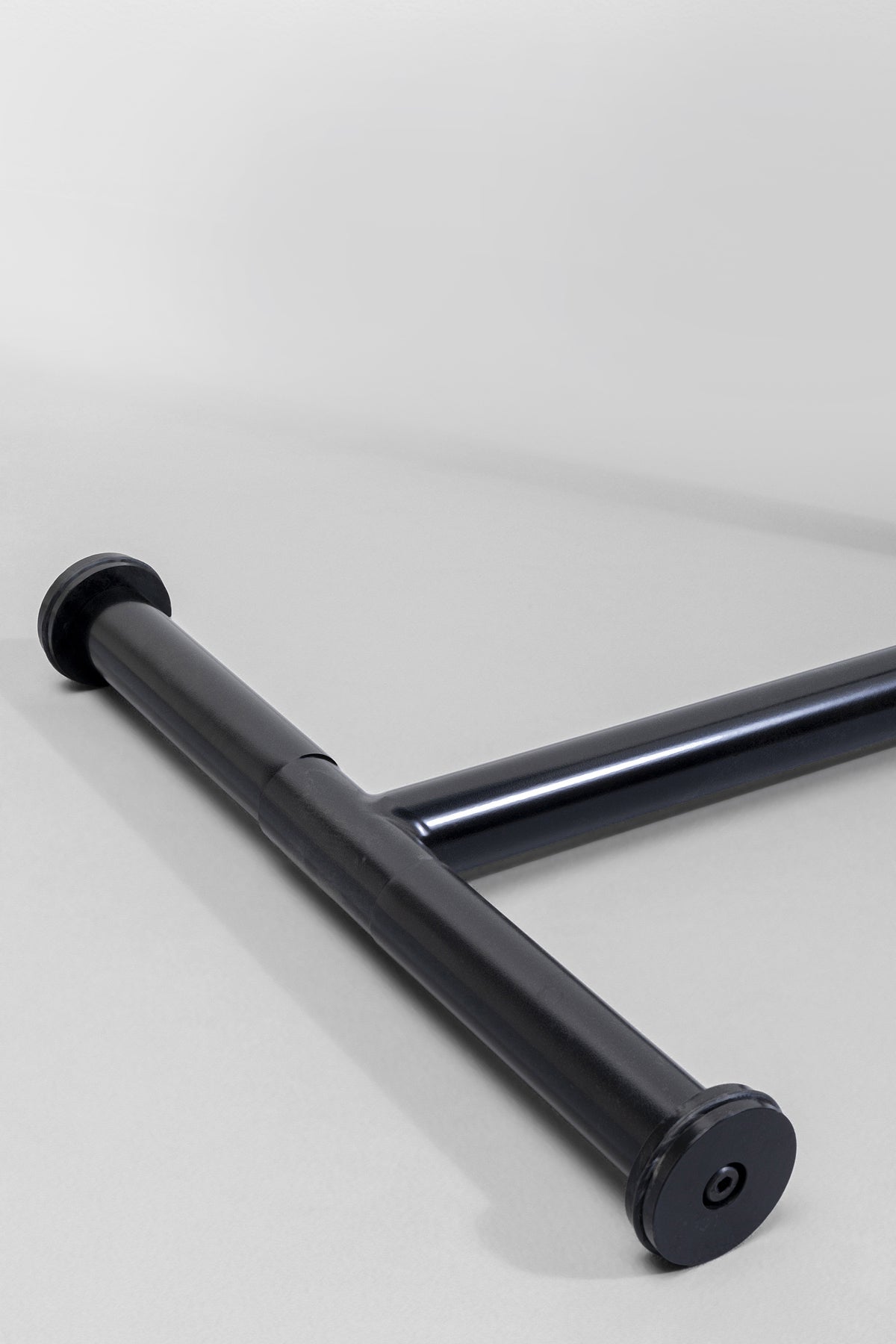 Eine Nahaufnahme des schwarzen T-förmigen Metallbeins des Beistelltischs Easy Living Schwarz Ø46cm, perfekt für den multifunktionalen Einsatz, präsentiert vor einem schlichten hellgrauen Hintergrund.