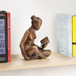 Bronzeskulptur einer sitzenden Frau, die ein Buch liest, auf einem Regal zwischen mehreren Büchern platziert.