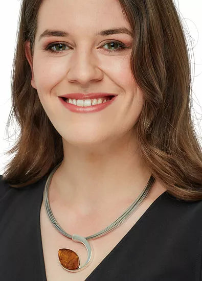 Lächelnde Frau mit schulterlangem braunem Haar in einem schwarzen Top, trägt das Bernsteincollier „Sylt“ – eine silberne Halskette mit einem braunen Anhänger.