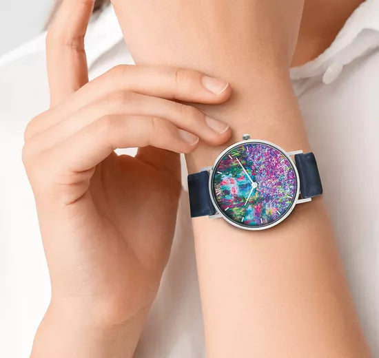 Person, die eine Uhr mit einem farbenfrohen, abstrakten Zifferblatt und einem dunkelblauen Armband trägt.