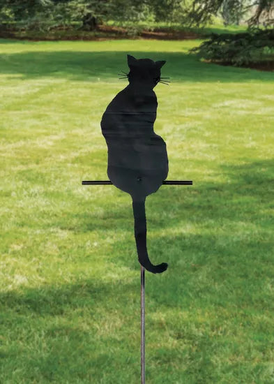Der Gartenstecker / die Silhouette „Sitzende Katze“ zeigt die Silhouette einer schwarzen Katze auf grünem Gras mit Bäumen im Hintergrund.