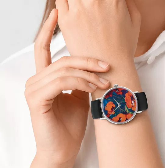 Eine Person trägt die Künstler-Armbanduhr „Emil Nolde – Großer Mohn (Rot, Rot, Rot)“ mit farbenfrohem Blumenmuster und schwarzem Band am Handgelenk.