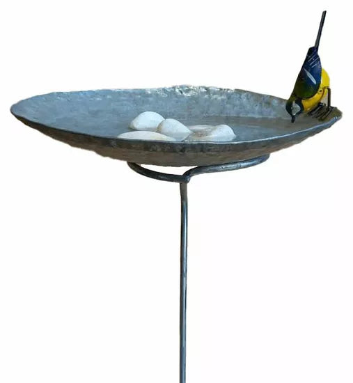 Ein Gartenstecker/Vogelbad mit Meise zeigt einen gelb-blauen Vogel, der aus einem flachen Vogelbad aus Metall mit weißen Steinen darin trinkt.