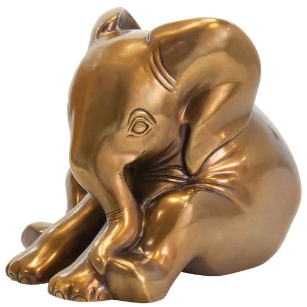 Eine kleine, goldfarbene Elefantenfigur, die mit einem unter dem Kopf zusammengerollten Rüssel sitzt.