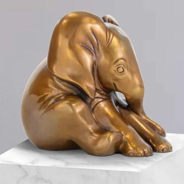 Eine Bronzeskulptur eines sitzenden Elefantenbabys auf einem weißen Marmorsockel.