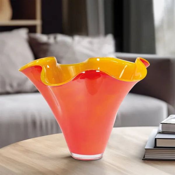 Eine leuchtend orangefarbene und gelbe gewellte Glasvase steht auf einem Holztisch in einem modernen Wohnzimmer.
