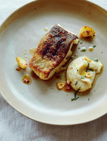 Ein Teller mit gebratenem Fisch, Kartoffelpüree, Röstkartoffeln und einem Spritzer Soße.