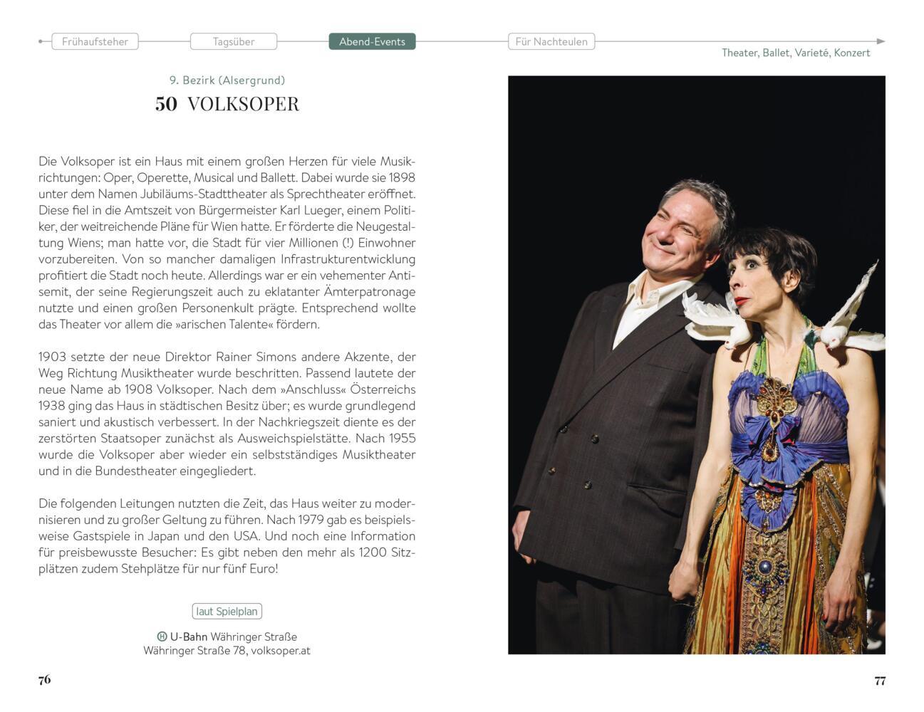 Ein Mann im Anzug und eine Frau in einem farbenfrohen Kleid posieren gemeinsam auf einer Theaterbühne und lächeln sich freundlich an.