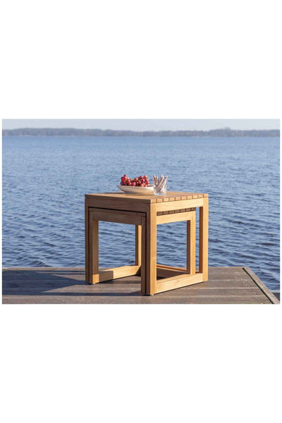 Ein Holztisch mit einer Schale mit Erdbeeren und Stöcken steht auf einem Steg an einem ruhigen Gewässer, in der Ferne sind Bäume zu sehen.