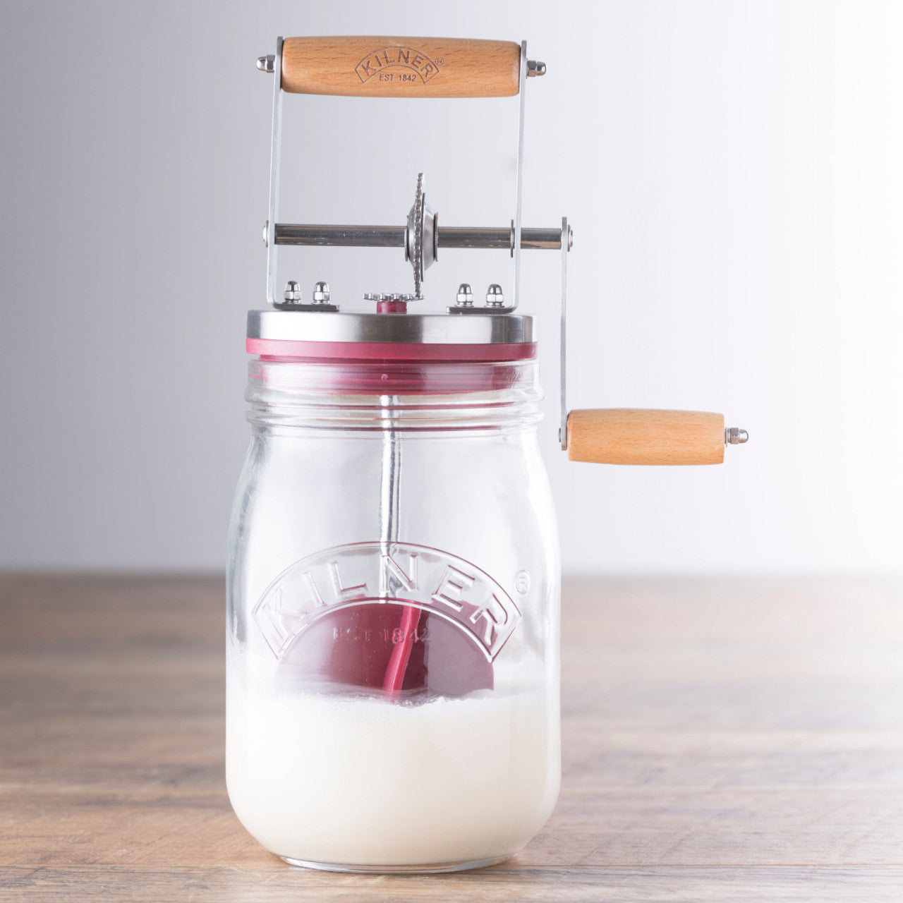 Das Butter Fass 1 Liter ist eine Buttermaschine mit Handkurbel, einem Glasbehälter, einem Metalldeckel und Holzgriffen und fasst bis zu einem Liter Sahne.