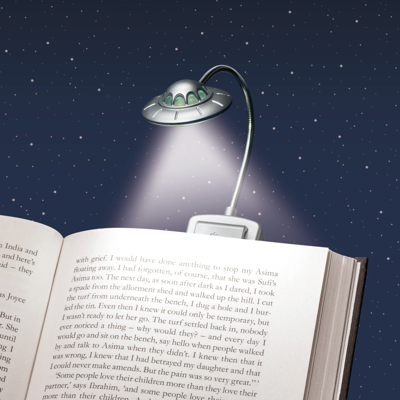 Die Leselampe UFO - 3 LEDs in UFO-Form beleuchten ein offenes Buch unter einem sternenklaren Nachthimmel.