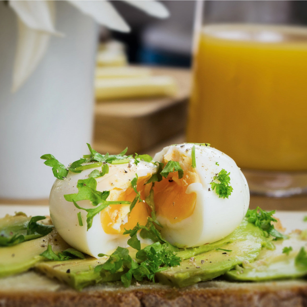 Avocado-Toast mit weichgekochten Eiern aus dem Goldenen PiepEI, garniert mit frischen Kräutern, serviert mit einem Glas Orangensaft.