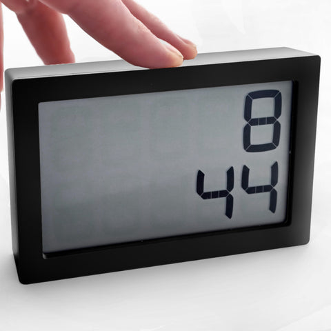 Eine Hand berührt eine Digitaluhr, die die Zeit 8:44 auf weißem Hintergrund anzeigt.