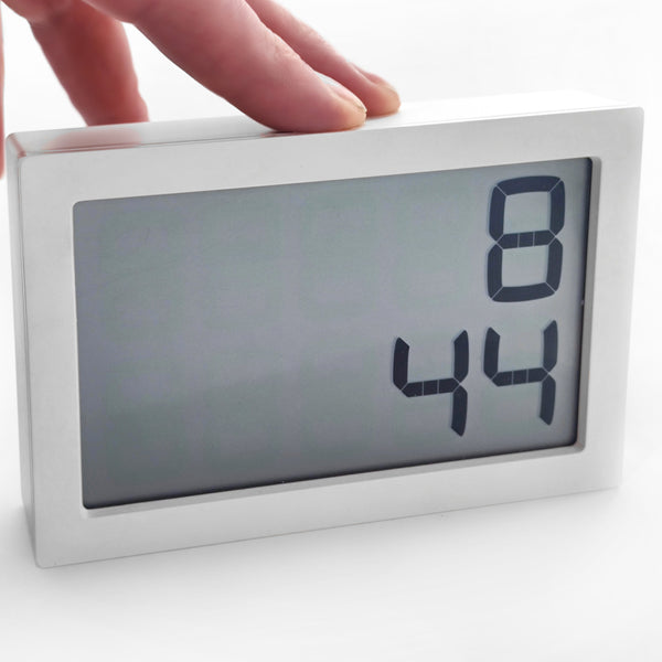 Eine Hand berührt eine Digitaluhr, die die Zeit 8:44 auf weißem Hintergrund anzeigt.