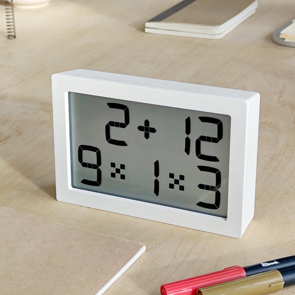 Eine Digitaluhr zeigt die Zeit mit mathematischen Gleichungen anstelle von Zahlen auf einem hölzernen Schreibtisch mit Schreibwaren in der Nähe an.