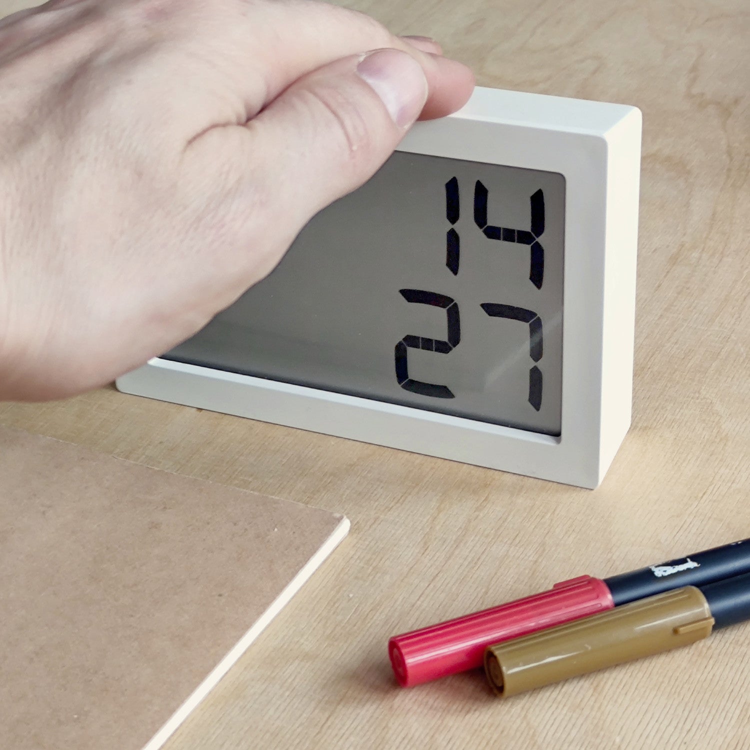 Eine Hand stellt eine Digitaluhr auf einem Schreibtisch ein, auf dem Stifte und ein Notizbuch liegen.
