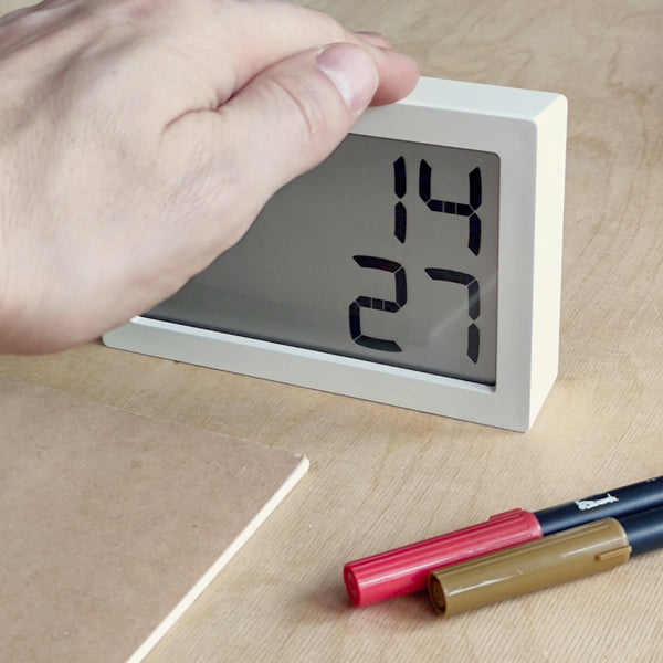 Eine Hand stellt eine Digitaluhr auf einem Schreibtisch ein, auf dem Stifte und ein Notizbuch liegen.