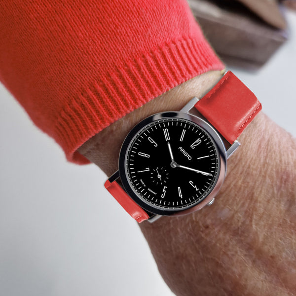 Eine Person, die eine Armbanduhr mit schwarzem Gesicht und rotem Armband und einen roten langärmeligen Pullover trägt.