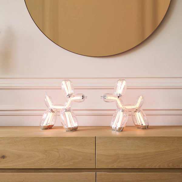 Zwei Lampen in Form von Ballonhunden auf einer Holzkommode unter einem runden Spiegel.